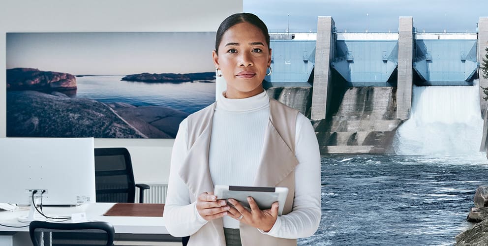 Frau hält Tablet in der Hand. Der Hintergrund zeigt ein Büroraum und eine Wasserkraftanlage.
